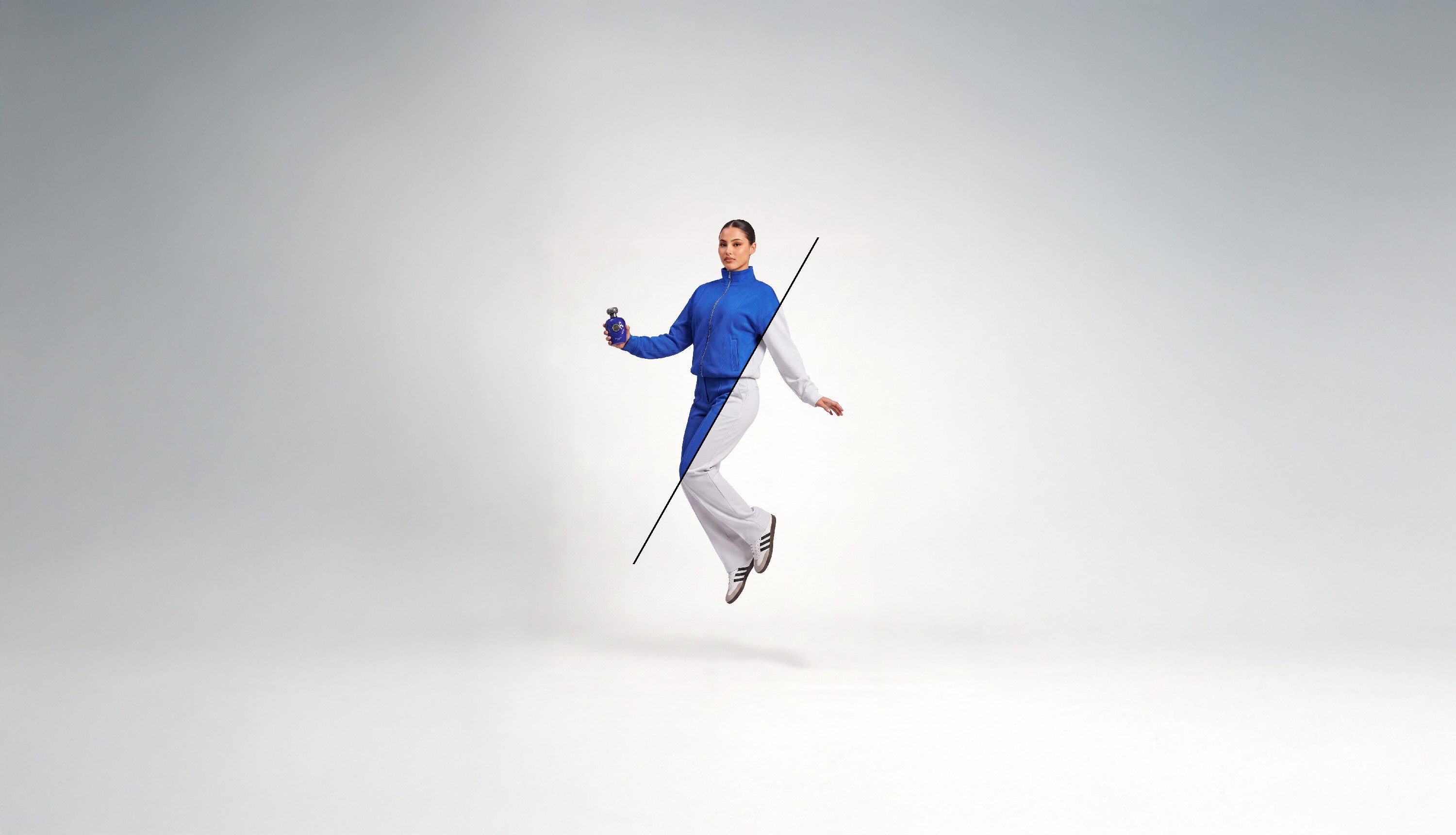 Model in a blue and white tracksuit, jumping, holding a bottle of Blue Oud